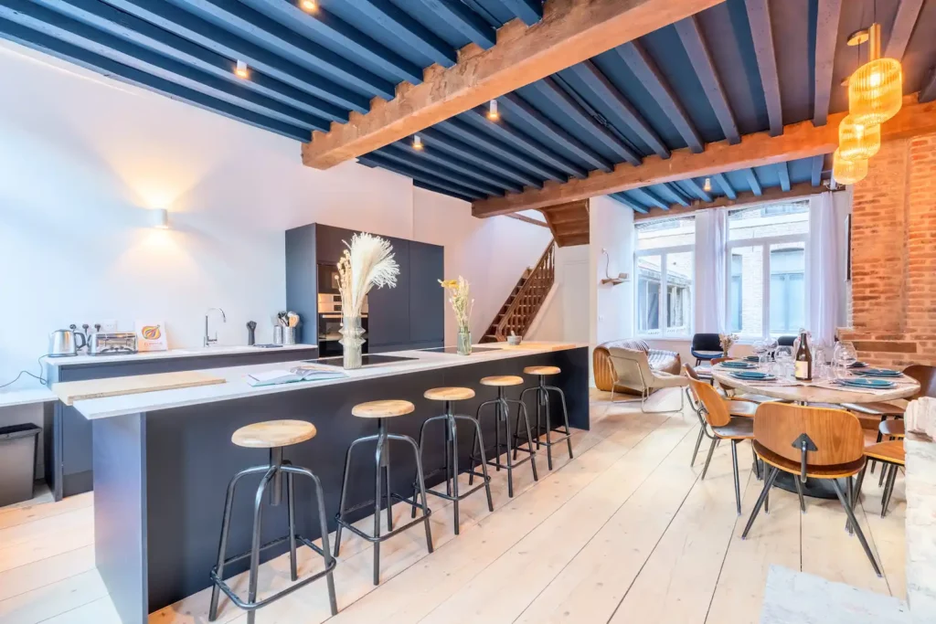 Cuisine avec îlot noir, tabourets et poutres bleues au plafond — Maison 3 Mollettes, coliving IvyNest dans le Vieux-Lille