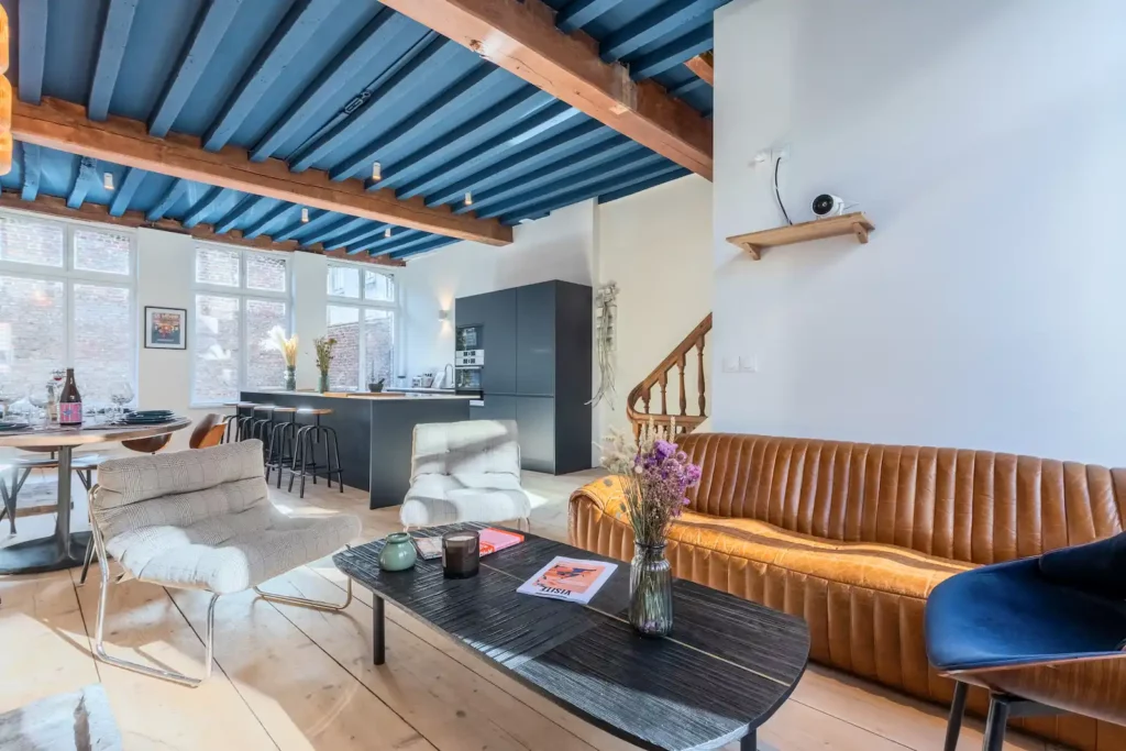 Salon avec canapé en cuir, table basse noire et poutres bleues — Maison 3 Mollettes, coliving IvyNest dans le Vieux-Lille