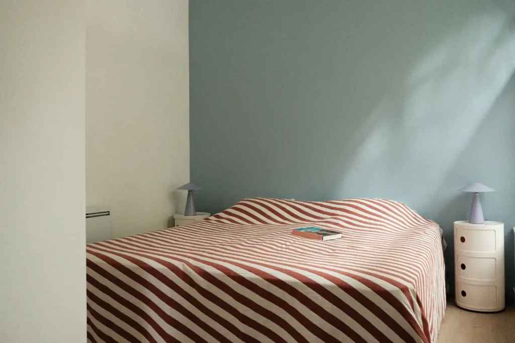 Chambre aux murs bleu-gris avec grand lit à couvre-lit rayé — Maison Bonte-Pollet, coliving IvyNest à Lille Vauban