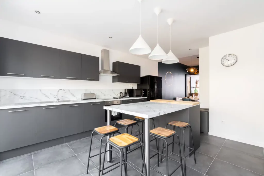 Cuisine grise avec îlot en marbre, tabourets en bois et suspensions — Maison Caumartin, coliving IvyNest à Lille Centre