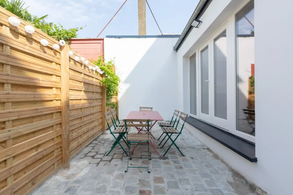 Patio étroit avec palissade en bois, guirlande lumineuse et table — Maison Caumartin, coliving IvyNest à Lille Centre