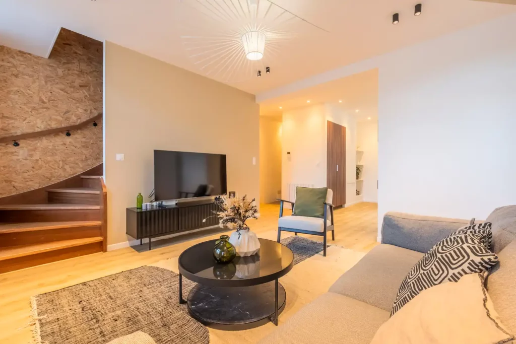 Salon avec canapé, table basse ronde et escalier tournant en bois — Maison Centre, coliving IvyNest à La Madeleine