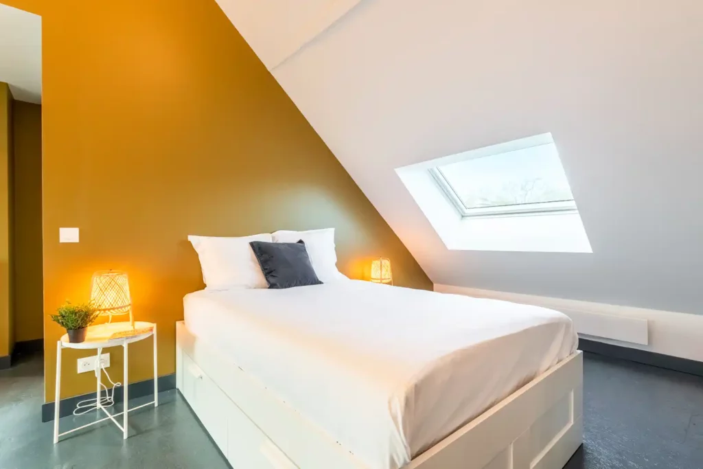 Chambre mansardée avec mur moutarde et fenêtre de toit — Maison Saint-Maurice, coliving IvyNest à Lille Saint-Maurice