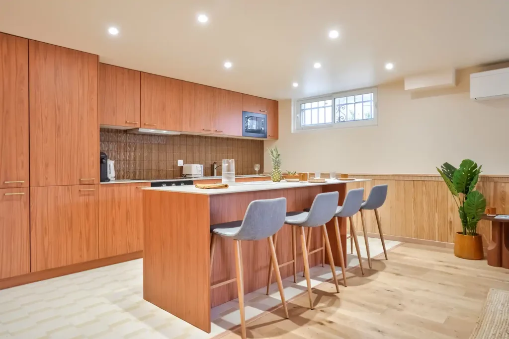 Cuisine avec hautes armoires en bois, îlot et tabourets gris — Maison Villejuif Hamon, coliving IvyNest à Villejuif