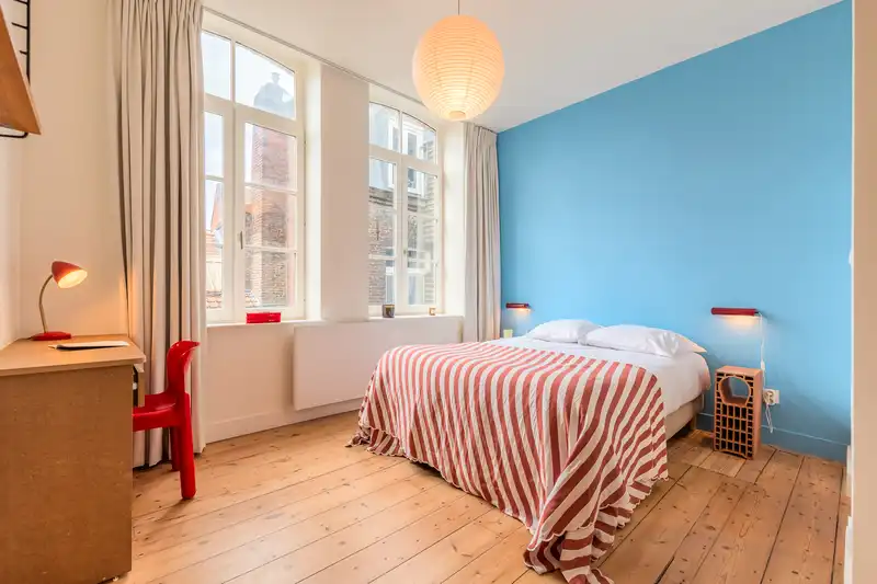 Chambre bleue avec bureau, lampe rouge et lit double rayé — Maison Rousseau, coliving IvyNest dans le Vieux-Lille