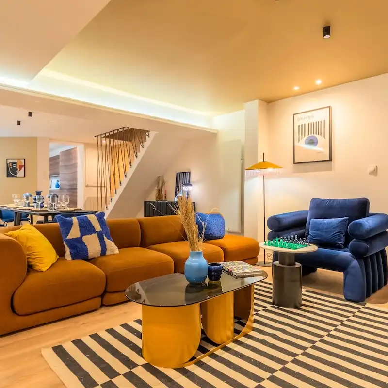 Salon avec canapé moutarde, fauteuil bleu et tapis rayé — Maison Nationale, coliving IvyNest à Lille Vauban