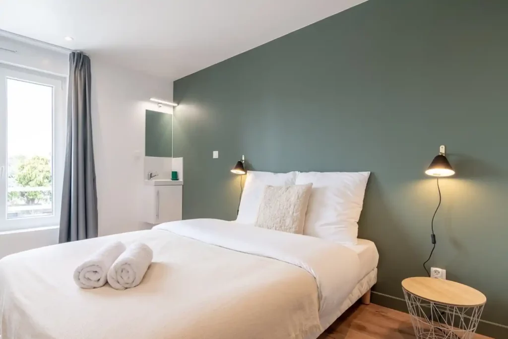 Chambre avec mur vert, lit double, serviettes roulées et lavabo — Maison Bourg, coliving IvyNest à Lomme