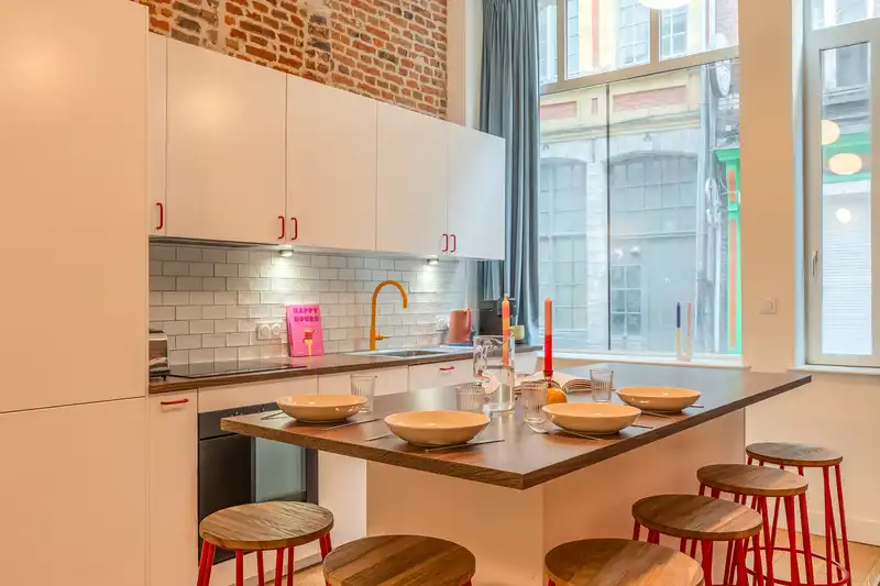 Cuisine à crédence blanche, îlot et tabourets rouges sous fenêtres — Maison Rousseau, coliving IvyNest dans le Vieux-Lille