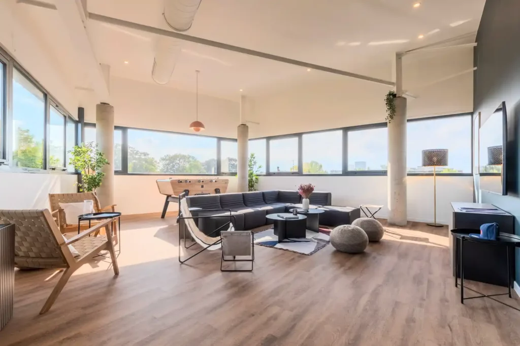 Grand séjour loft avec canapé d'angle gris, baby-foot et baies vitrées — Maison Sainte-Hélène, coliving IvyNest à Saint-André