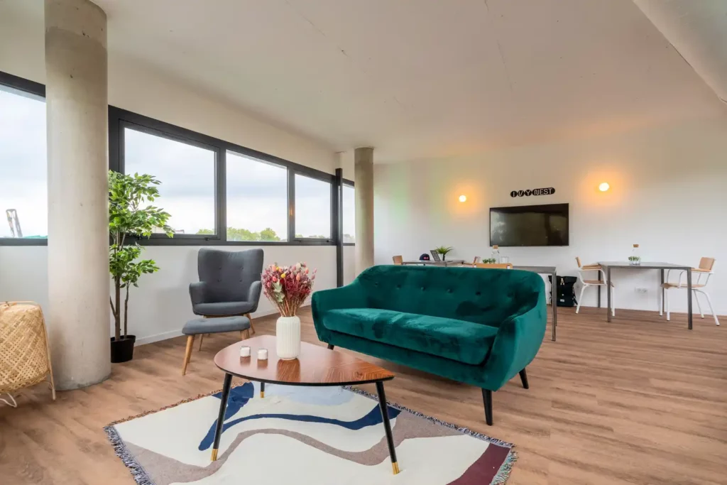 Salon avec canapé vert émeraude, fauteuil gris et poteaux en béton — Maison Sainte-Hélène, coliving IvyNest à Saint-André