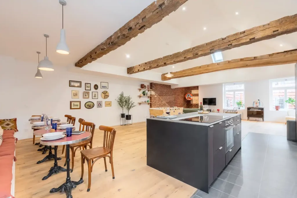 Séjour sous poutres avec îlot noir et tables bistrot — Maison Sainte-Catherine, coliving IvyNest dans le Vieux-Lille