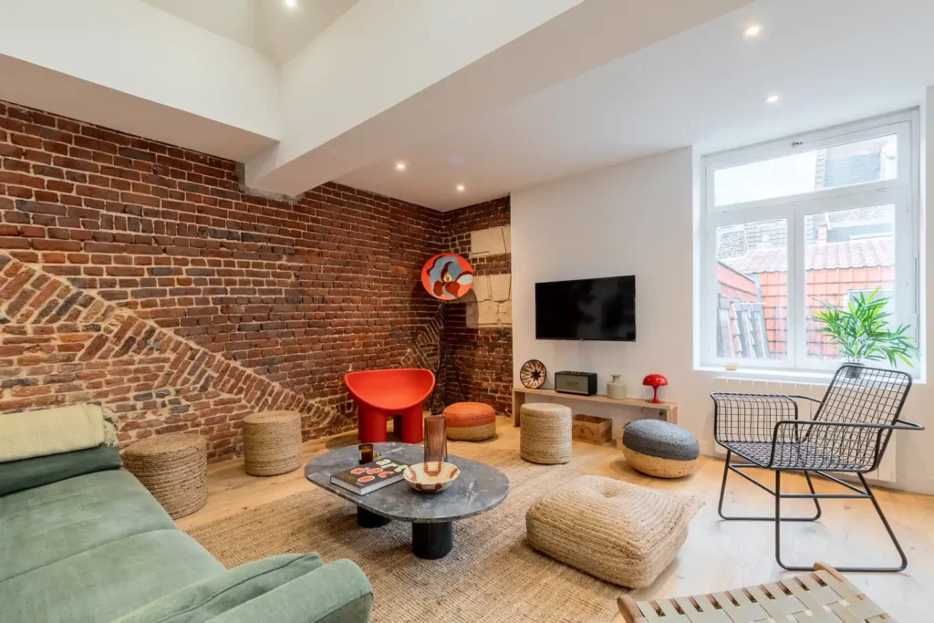 Salon en briques avec canapé vert et fauteuil rouge design — Maison Sainte-Catherine, coliving IvyNest dans le Vieux-Lille