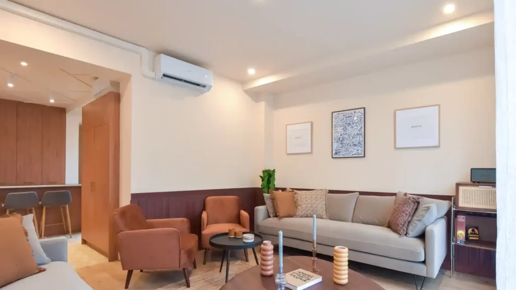 Salon avec canapé gris, fauteuils terracotta et climatisation murale — Maison Cachan, coliving IvyNest à Cachan