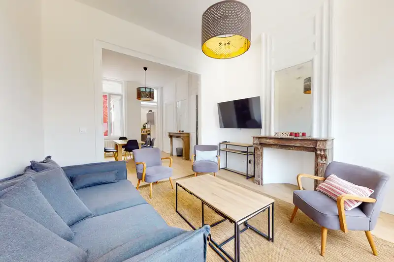 Grand salon avec canapé bleu gris et fauteuils, salle à manger au fond — Maison Artois, coliving IvyNest à Lille JB Lebas