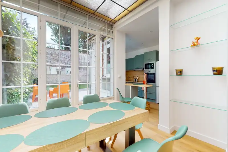 Véranda avec table en bois, chaises vertes et cuisine au fond — Maison 39 Bigo-Danel, coliving IvyNest à Lille Vauban