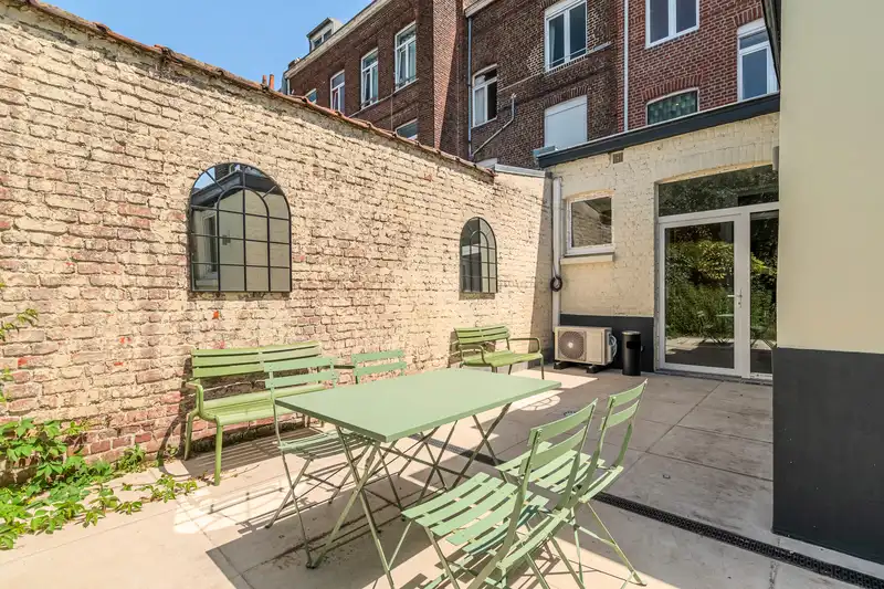 Terrasse en dalles avec table et chaises vertes, mur en briques — Maison 68 Roland, coliving IvyNest à Lille Vauban